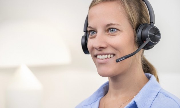 Person mit braunen Haaren, hellblauem Hemd und schwarzem Headset vor hellem Hintergrund.