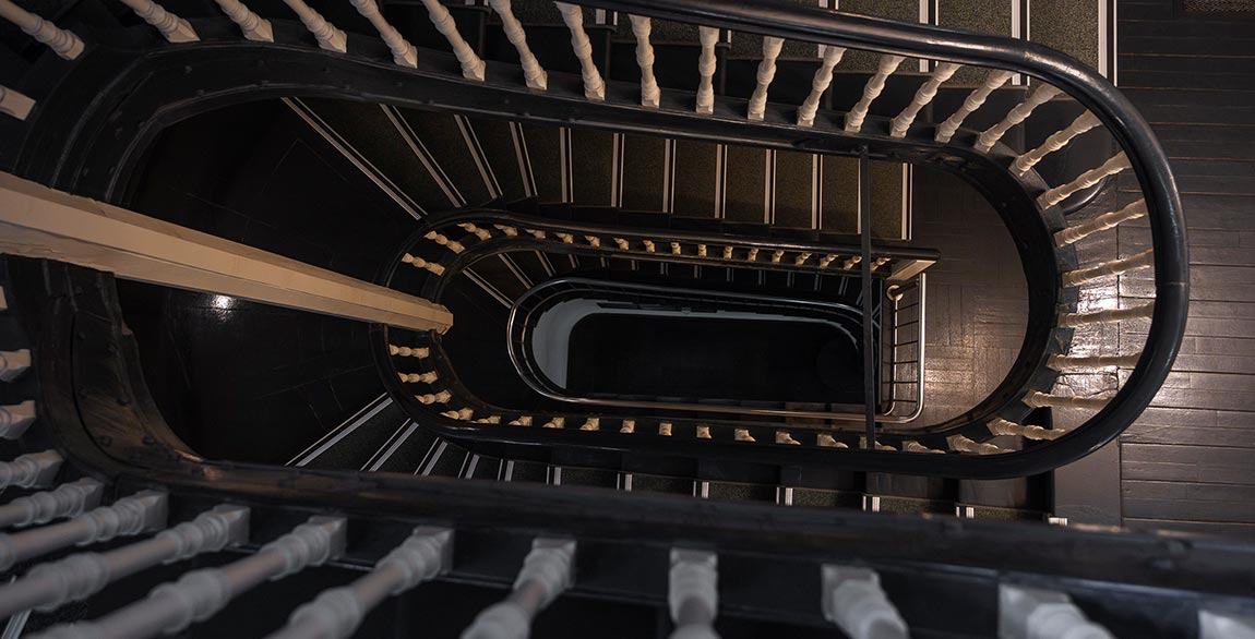 Blick von oben in ein ovales Treppenhaus mit dunklem Geländer und weißen Balustern.